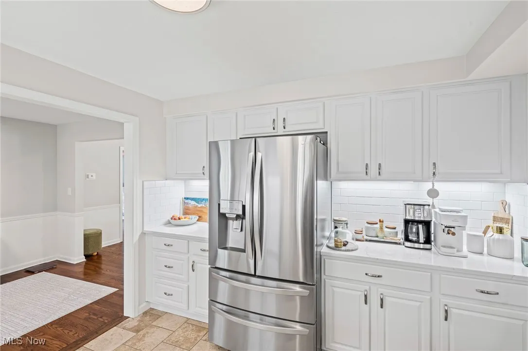 Kitchen with stainless steel fridge, tasteful backsplash, white cabinetry, and light wood finished floors