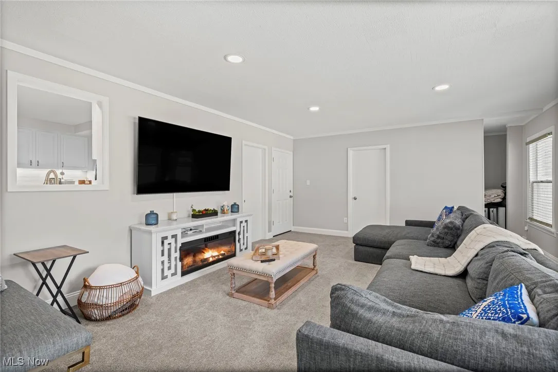 Carpeted living area with recessed lighting, ornamental molding, and a glass covered fireplace