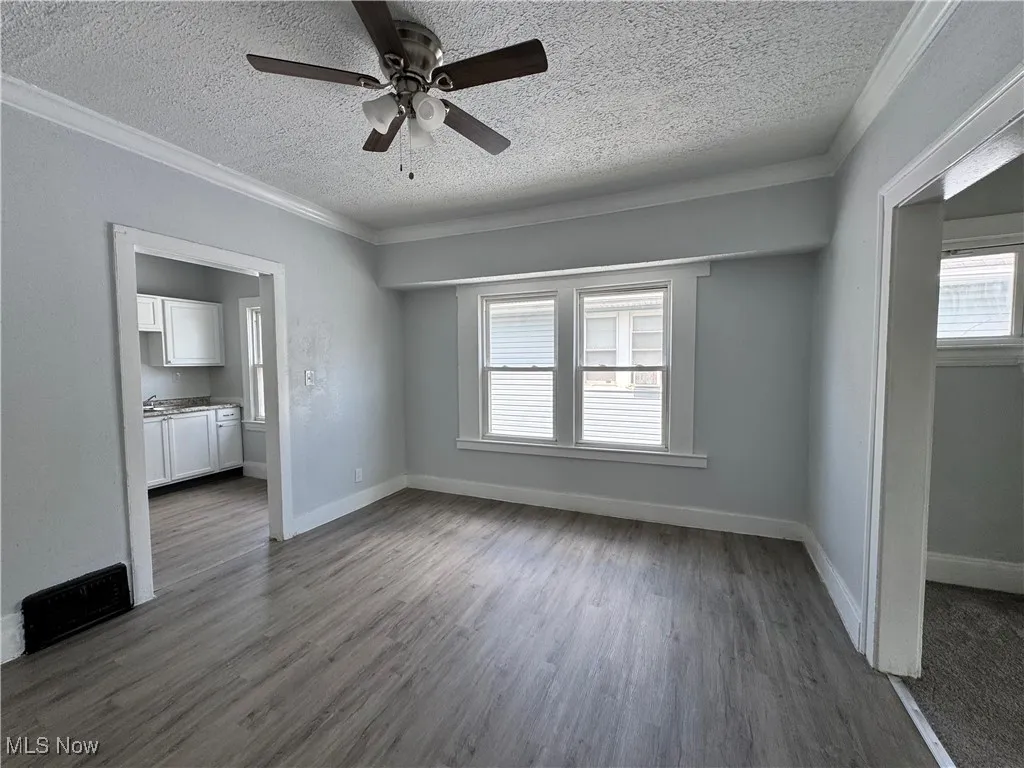 Unfurnished living room with a textured ceiling, a ceiling fan, crown molding, and dark wood-type flooring