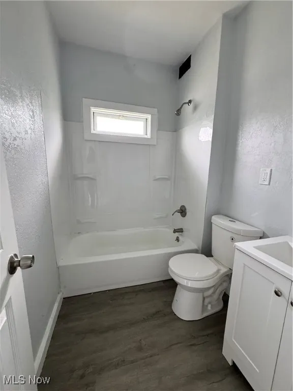 Bathroom with vanity, wood finished floors,  shower combination, and a textured wall
