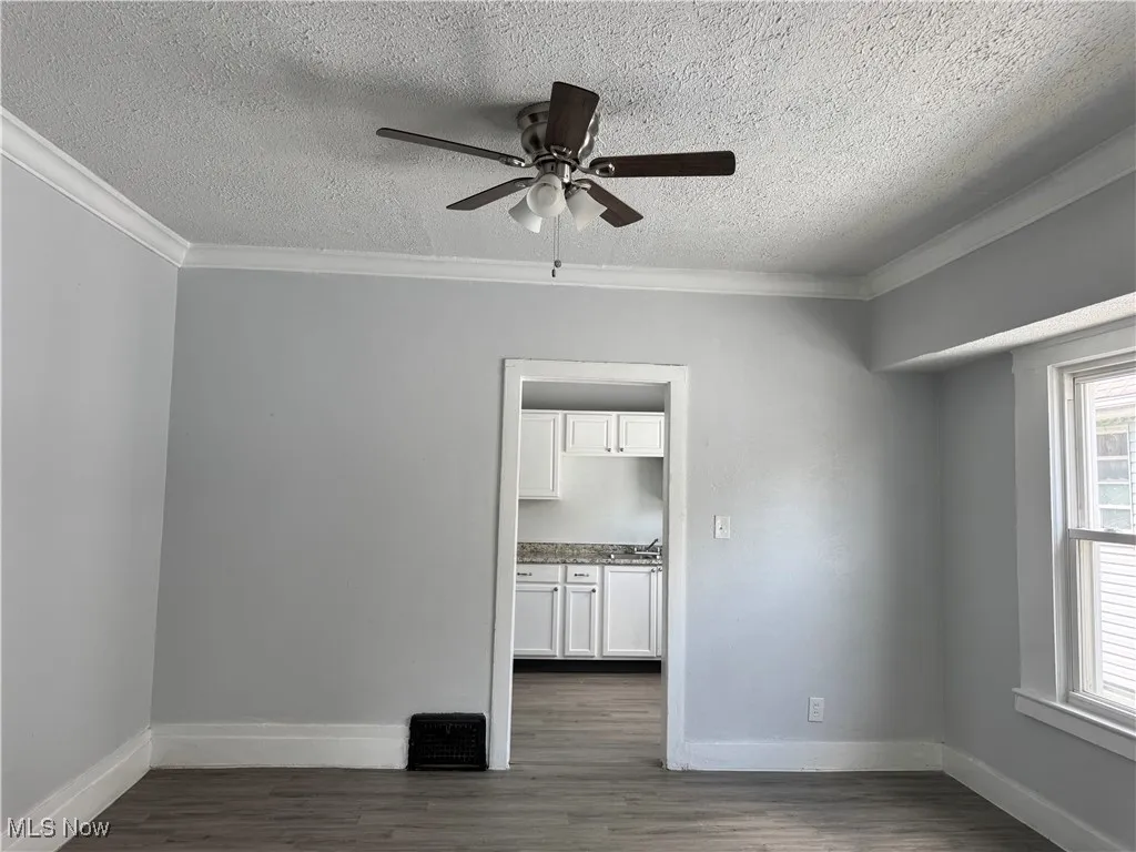 Spare room with a textured ceiling, a ceiling fan, ornamental molding, and dark wood-style floors