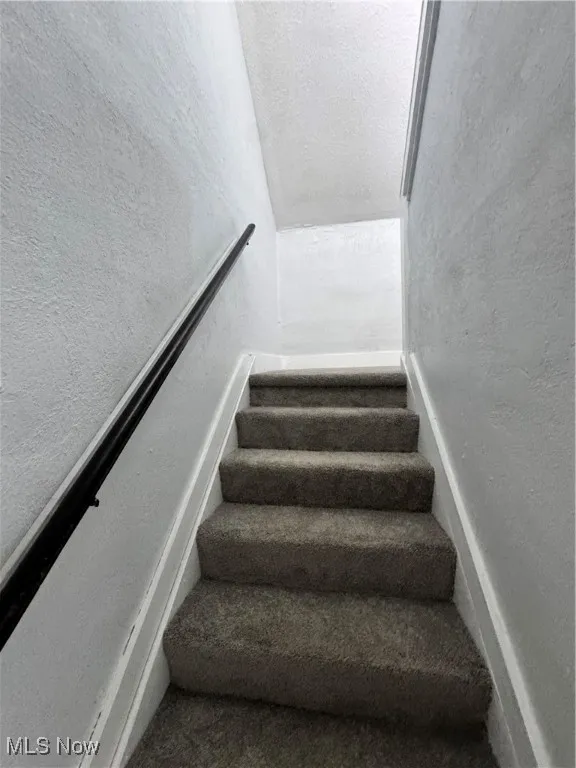 Stairway featuring lofted ceiling and a textured wall