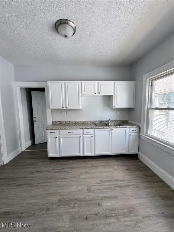 Kitchen with white cabinets, dark wood finished floors, a textured ceiling, and light stone countertops