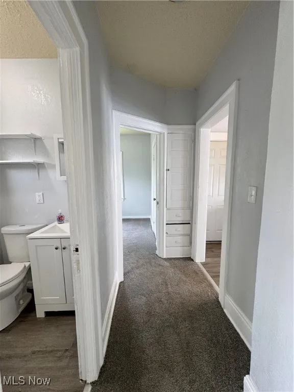 Hallway with a textured ceiling, carpet, and a textured wall