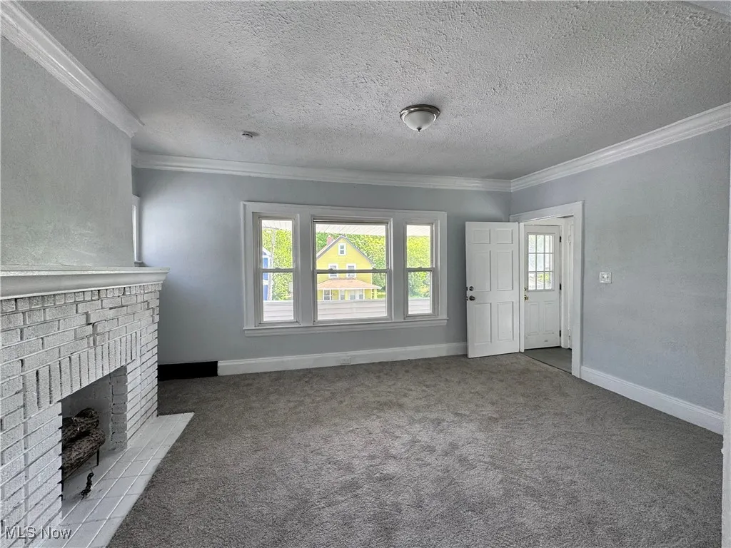 Unfurnished living room featuring crown molding, carpet floors, a textured ceiling, and a brick fireplace