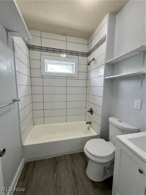 Bathroom featuring a textured ceiling, bathtub / shower combination, vanity, wood finished floors, and a textured wall