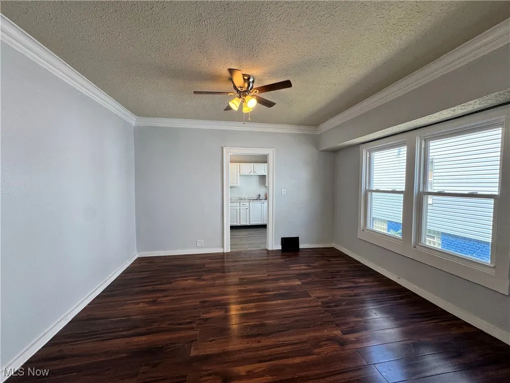 Spare room featuring wood finished floors, ornamental molding, a textured ceiling, and ceiling fan