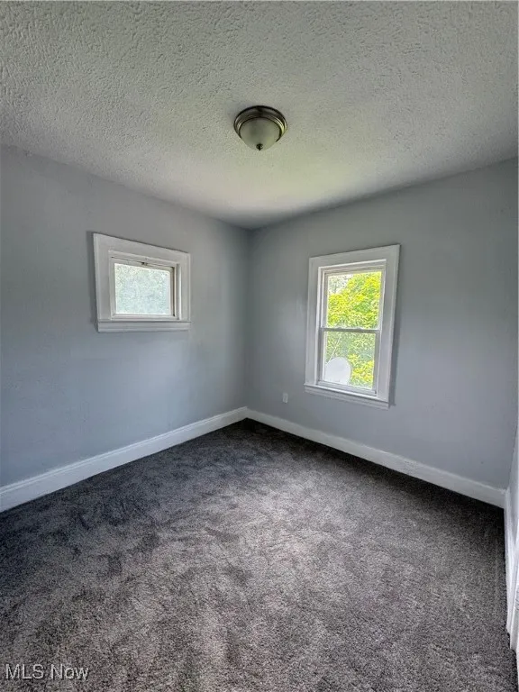 Empty room featuring plenty of natural light, dark carpet, and a textured ceiling