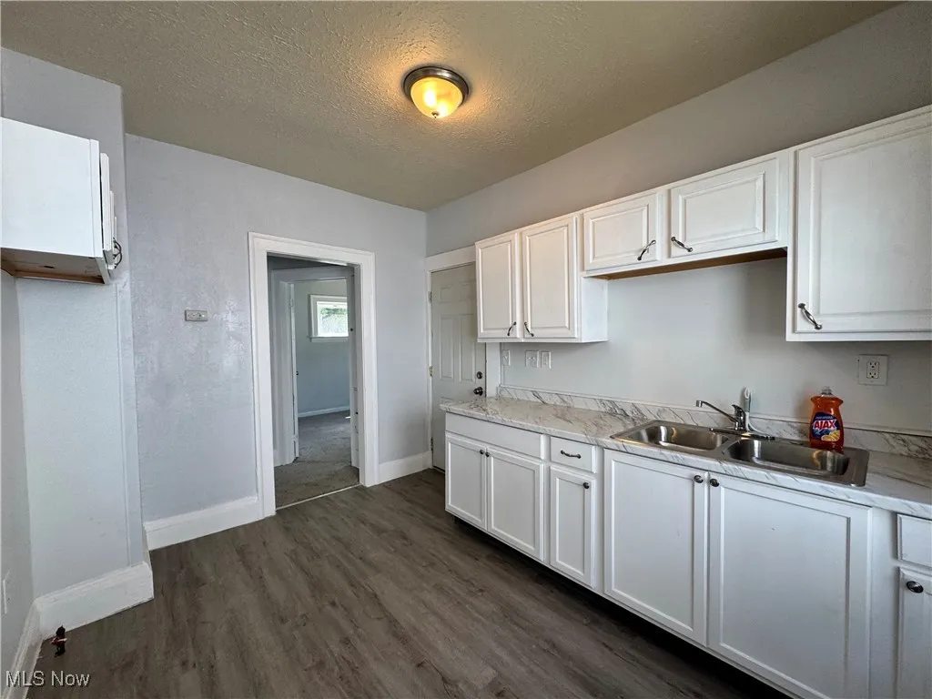 Kitchen with a textured ceiling, white cabinetry, light countertops, and dark wood-type flooring