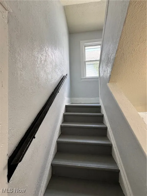 Staircase featuring a textured wall and a textured ceiling