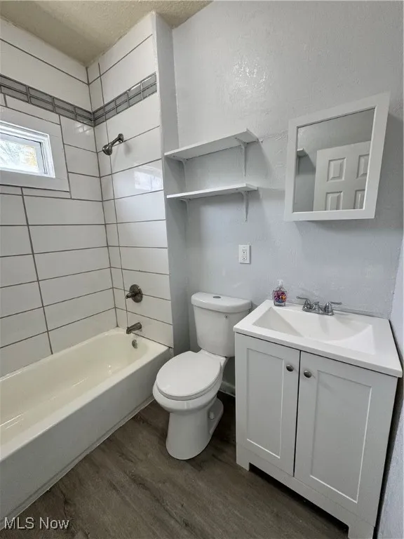 Bathroom with a textured ceiling, wood finished floors, vanity, and shower / bathtub combination