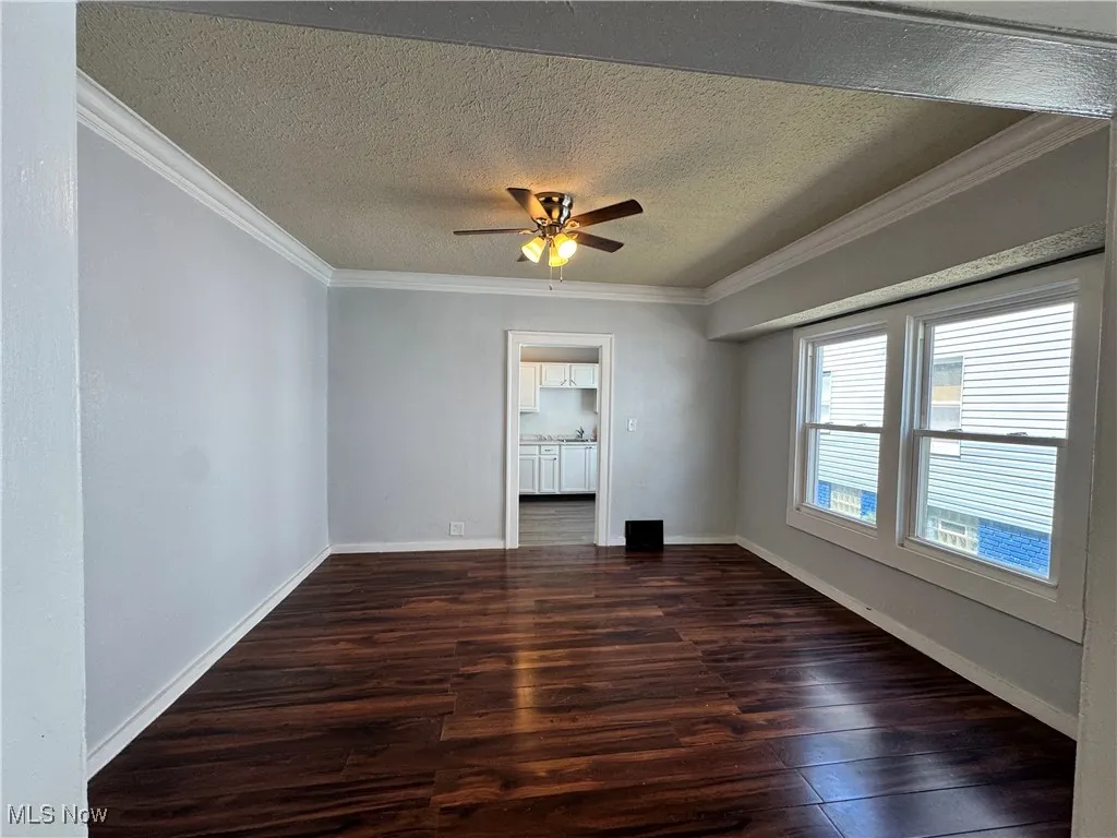 Empty room with crown molding, a textured ceiling, wood finished floors, and ceiling fan