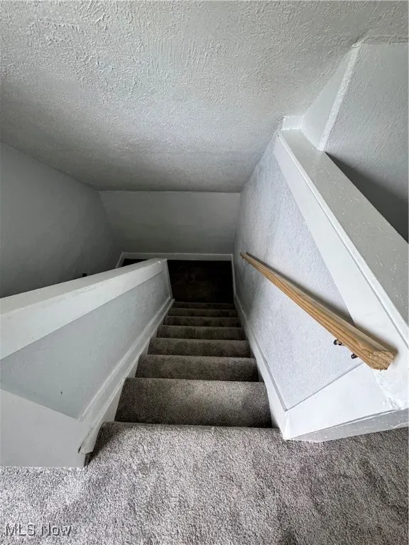 Stairway featuring a textured ceiling, carpet, and vaulted ceiling