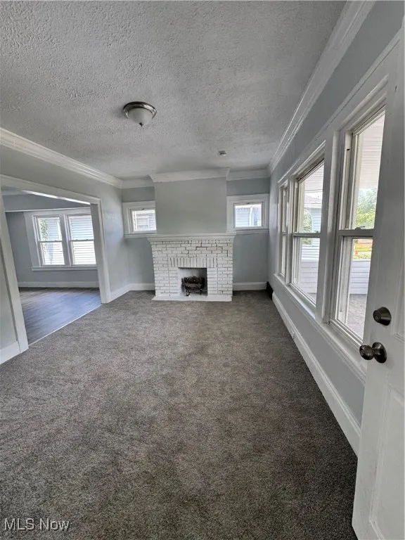 Unfurnished living room with crown molding, dark colored carpet, a fireplace, and a textured ceiling