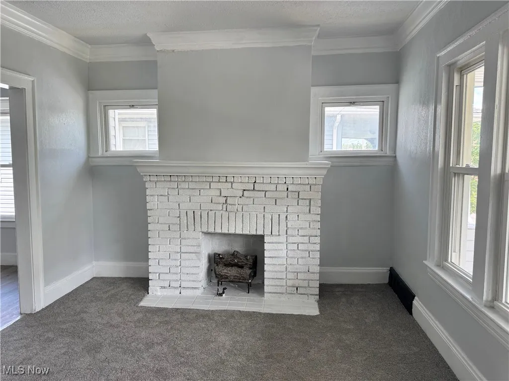 Detailed view of crown molding, a brick fireplace, carpet flooring, and a textured ceiling