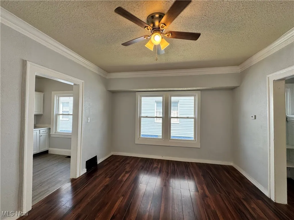 Unfurnished room with dark wood finished floors, a textured ceiling, ornamental molding, and ceiling fan