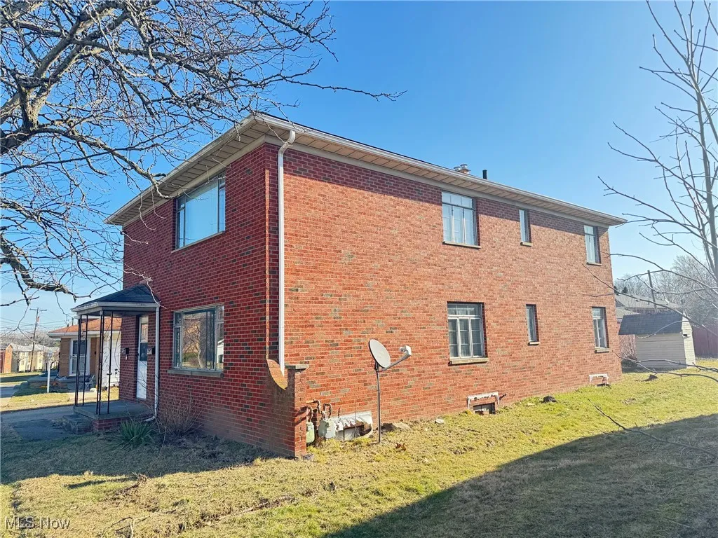 View of property exterior featuring brick siding and a lawn
