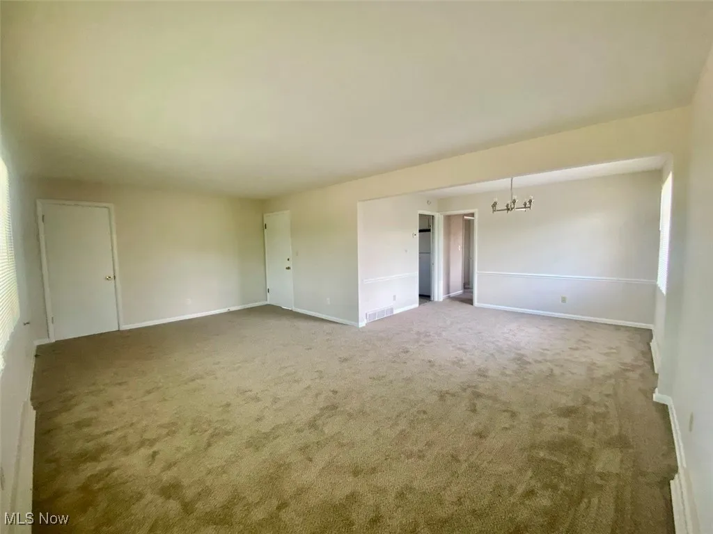 Carpeted empty room featuring a chandelier and baseboards