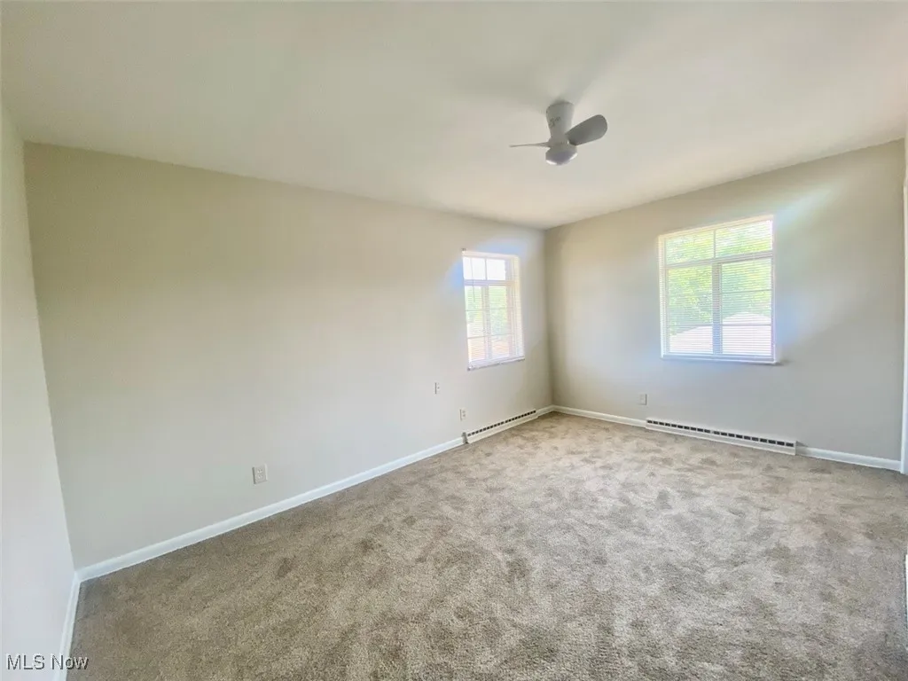 Carpeted empty room with plenty of natural light, a ceiling fan, and baseboard heating