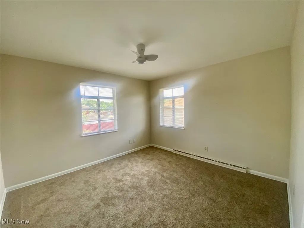 Unfurnished room featuring carpet, plenty of natural light, baseboard heating, and a ceiling fan