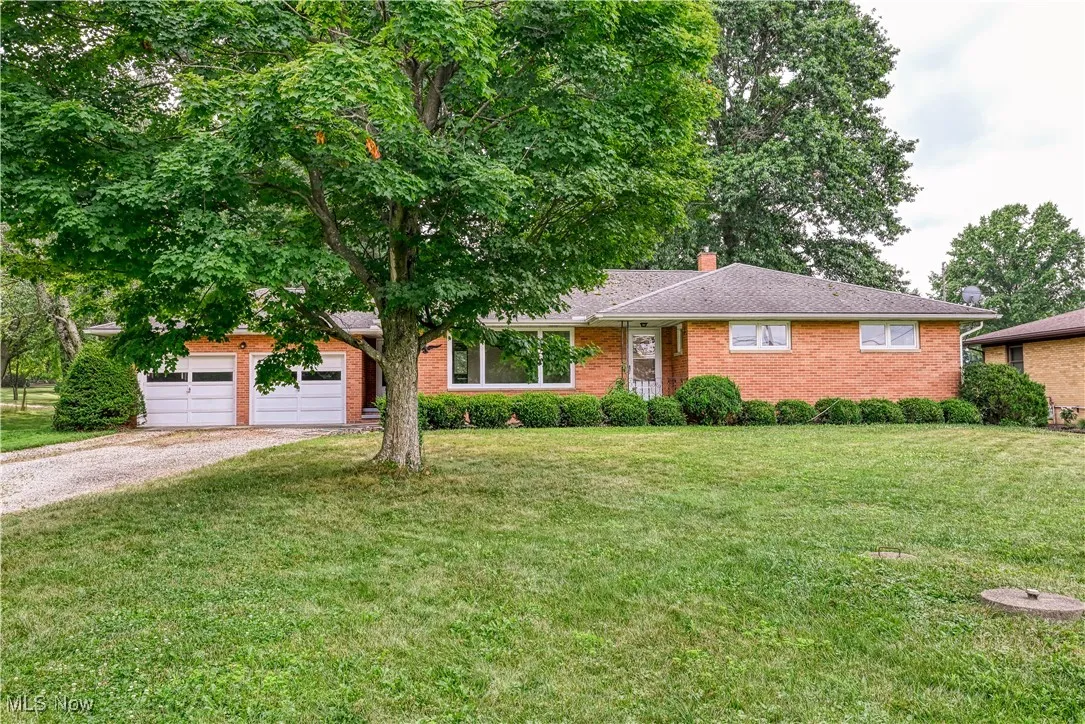 Ranch-style home featuring driveway, an attached garage, brick siding, a front lawn, and a chimney