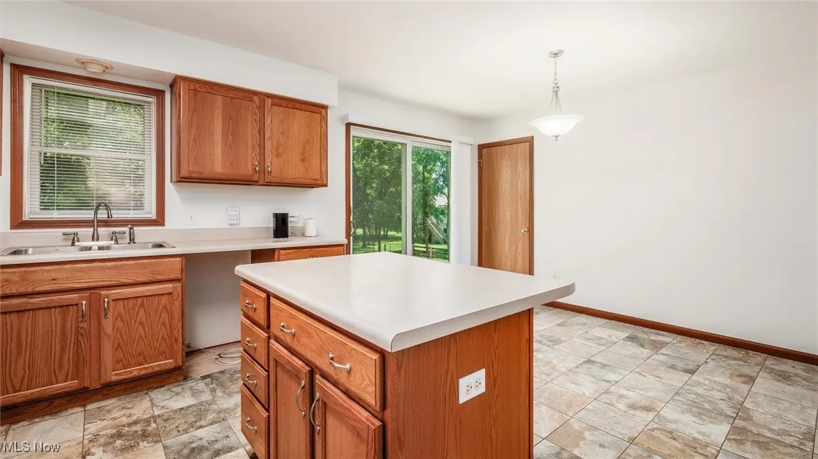 Kitchen featuring plenty of natural light, brown cabinets, light countertops, and decorative light fixtures