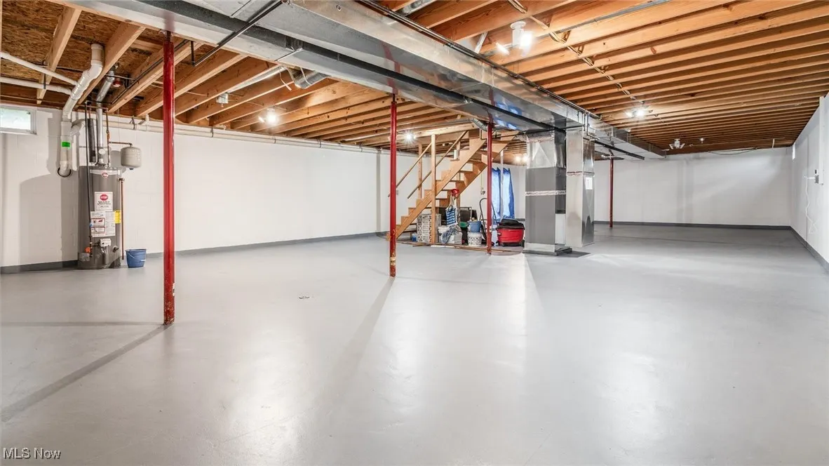 Unfinished below grade area featuring gas water heater, stairway, and heating unit