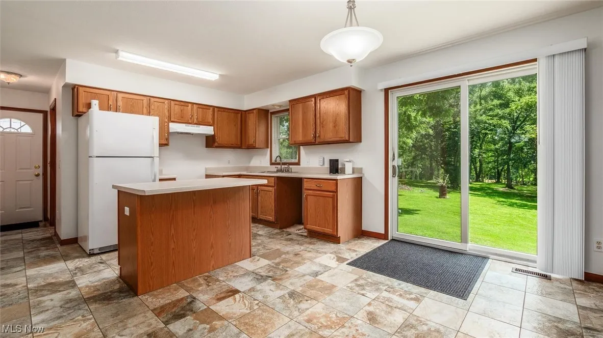 Kitchen with freestanding refrigerator, a center island, brown cabinetry, light countertops, and pendant lighting