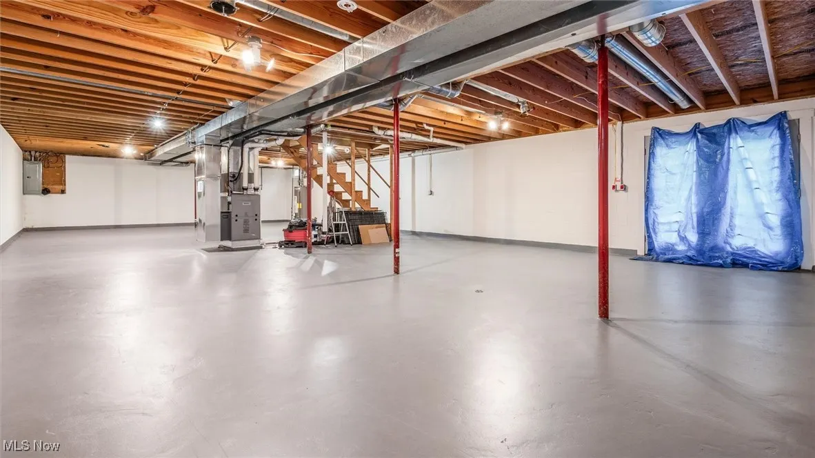 Unfinished below grade area with stairs, heating unit, electric panel, and concrete block wall