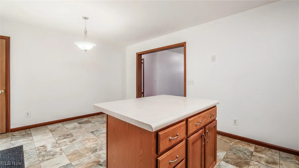 Kitchen featuring stone finish flooring, brown cabinets, light countertops, hanging light fixtures, and a center island