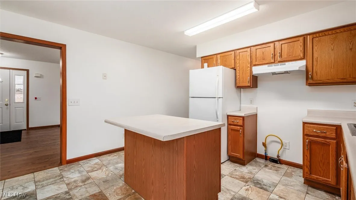 Kitchen featuring freestanding refrigerator, brown cabinets, light countertops, a kitchen island, and under cabinet range hood
