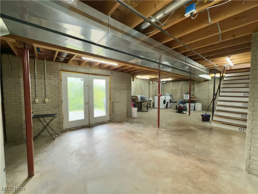 Basement featuring independent washer and dryer, stairway, brick wall, and french doors