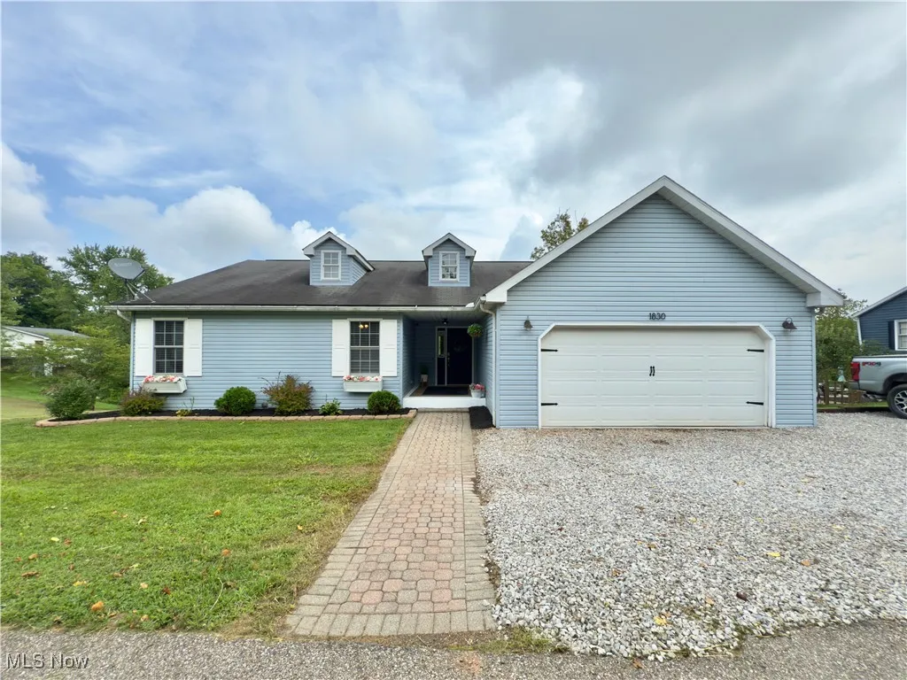 View of front of property with an attached garage, gravel driveway, and a front lawn