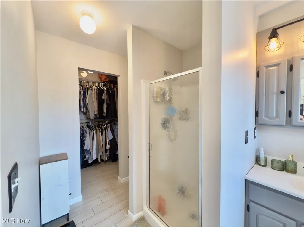 Full bath featuring a stall shower, vanity, wood finished floors, and a walk in closet