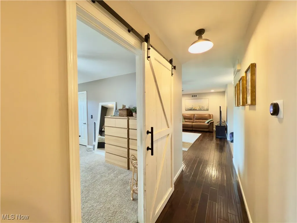 Hall with a barn door, dark wood-style flooring, and dark carpet
