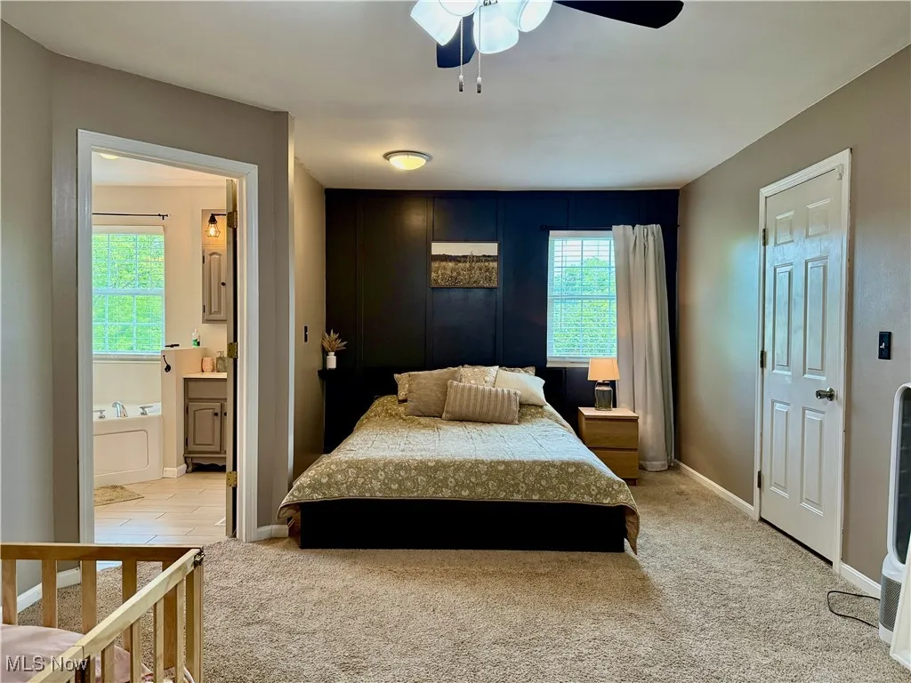 Bedroom featuring light carpet, multiple windows, connected bathroom, and ceiling fan
