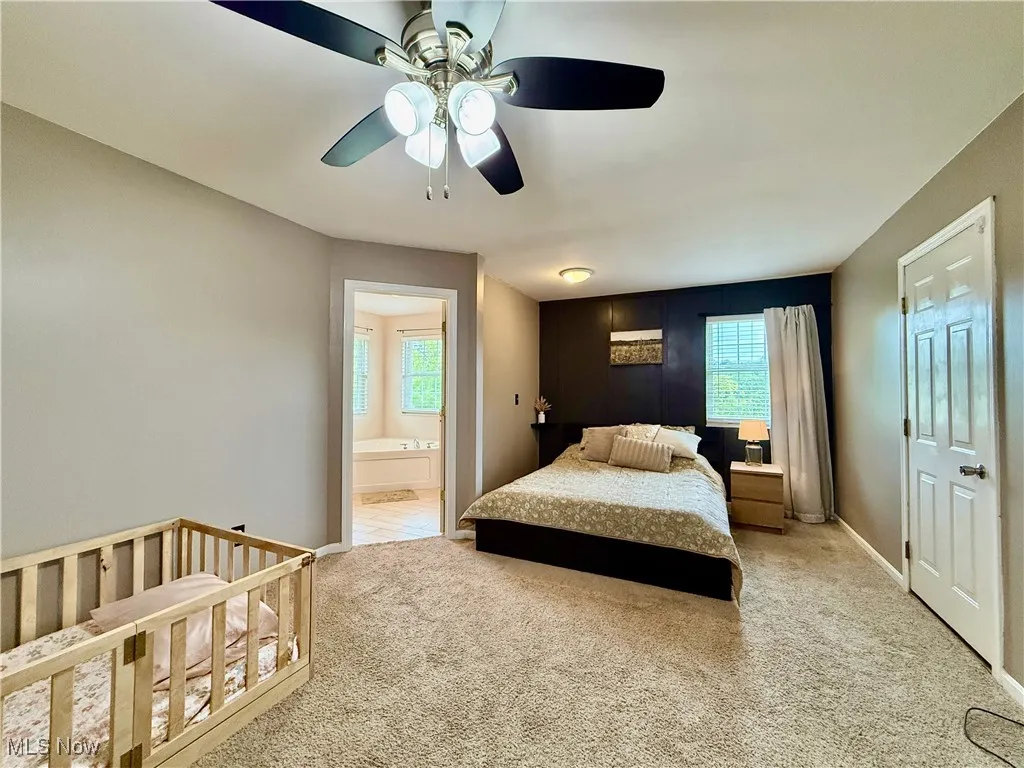 Carpeted bedroom featuring multiple windows, ceiling fan, and connected bathroom