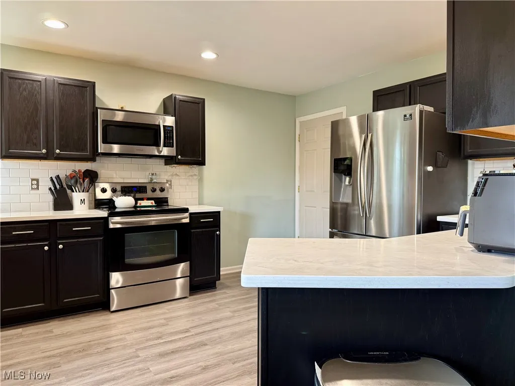 Kitchen featuring tasteful backsplash, stainless steel appliances, light countertops, light wood-style flooring, and recessed lighting