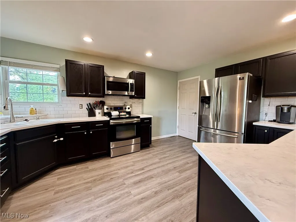 Kitchen featuring decorative backsplash, appliances with stainless steel finishes, light countertops, light wood-type flooring, and recessed lighting