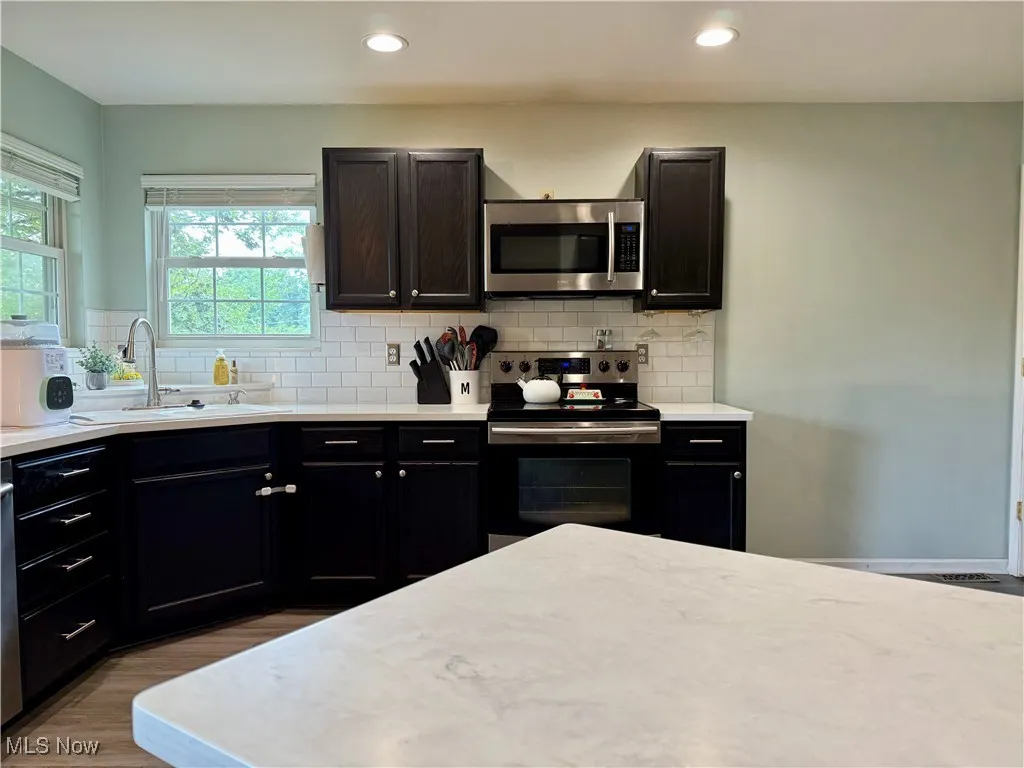 Kitchen with stainless steel appliances, light countertops, decorative backsplash, wood finished floors, and recessed lighting