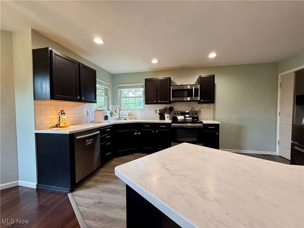 Kitchen with wood finished floors, appliances with stainless steel finishes, light countertops, decorative backsplash, and recessed lighting