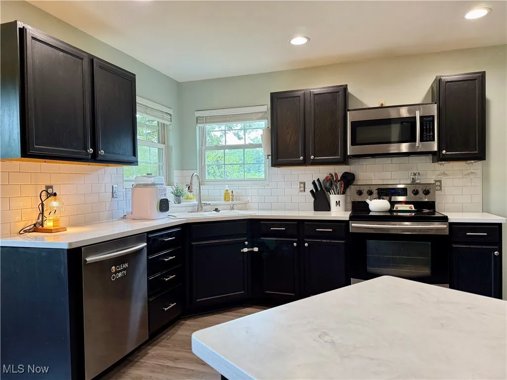 Kitchen featuring stainless steel appliances, decorative backsplash, light countertops, light wood finished floors, and recessed lighting