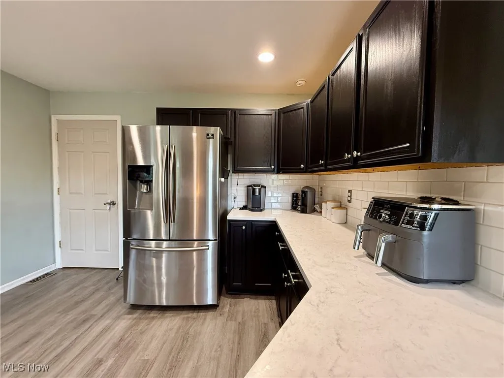 Kitchen featuring stainless steel fridge with ice dispenser, backsplash, light wood-type flooring, light stone countertops, and recessed lighting