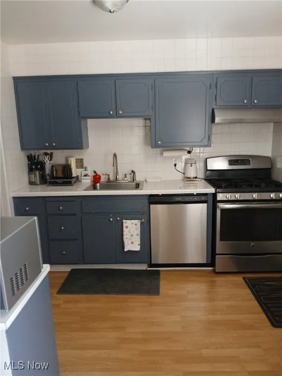 Kitchen featuring stainless steel appliances, light wood-style flooring, light countertops, backsplash, and under cabinet range hood