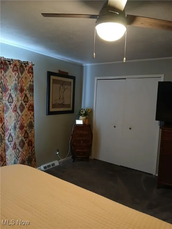 Bedroom with a closet, a ceiling fan, and dark carpet
