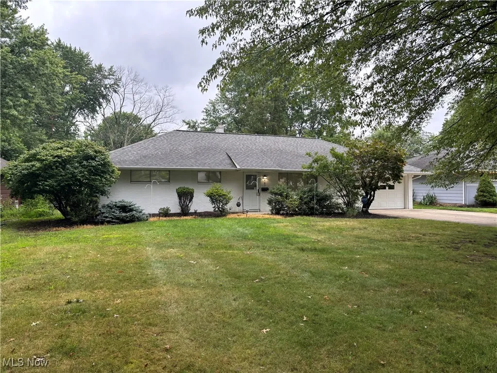Ranch-style home featuring driveway, roof with shingles, an attached garage, and a front yard