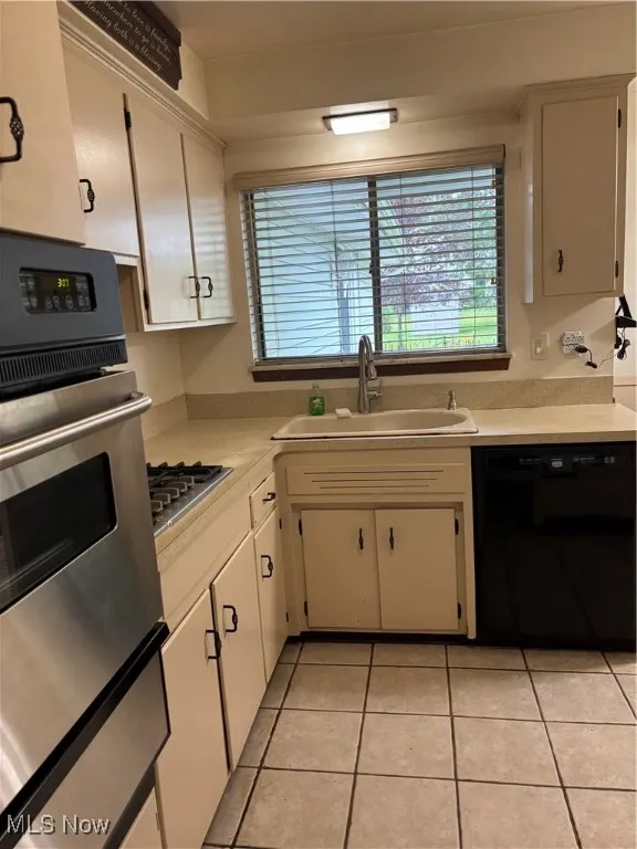 Kitchen featuring wall oven, dishwasher, light countertops, light tile patterned flooring, and stovetop