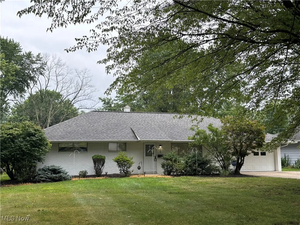 Ranch-style home featuring a shingled roof, a front yard, a chimney, a garage, and driveway