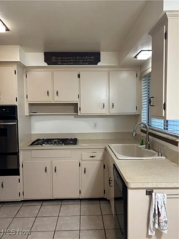 Kitchen featuring light countertops, wall oven, light tile patterned flooring, dishwashing machine, and white cabinets