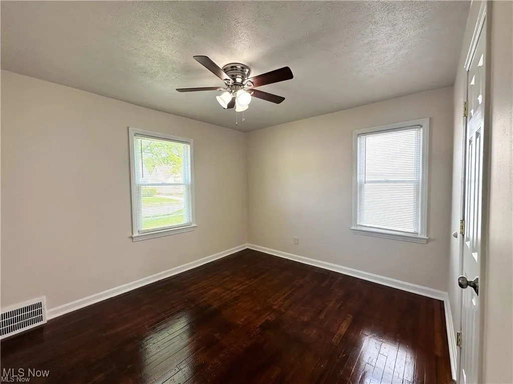 Empty room featuring dark wood-type flooring, a textured ceiling, and ceiling fan